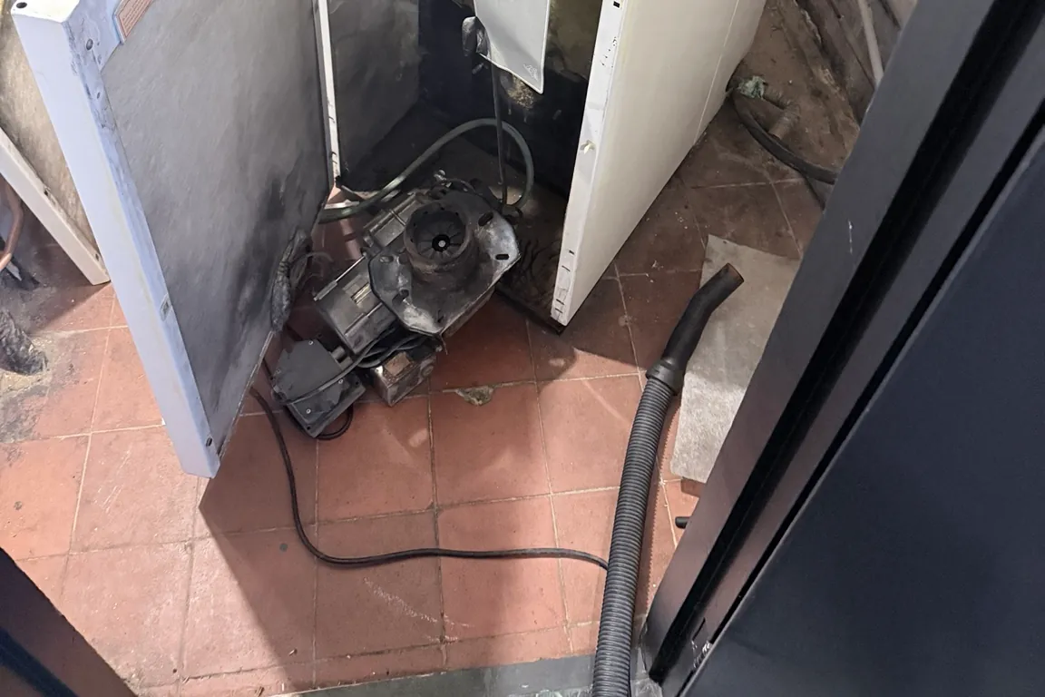 Oil burner removed and resting on the floor during a service, with the boiler cabinet open and a vacuum hose ready for cleaning