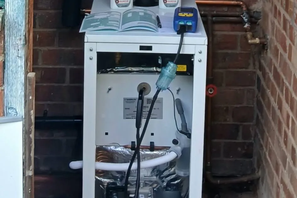 Oil boiler with its front panel removed, being tested with a combustion analyser