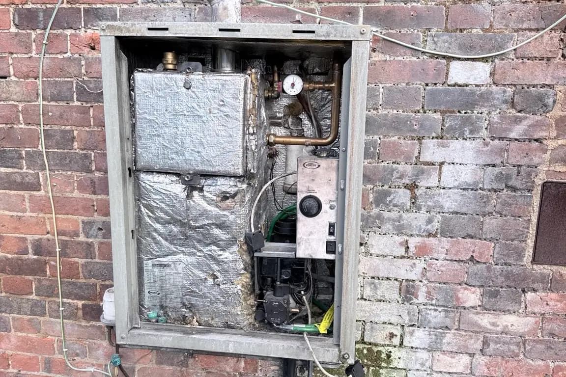 External wall-mounted oil boiler with its casing removed for maintenance