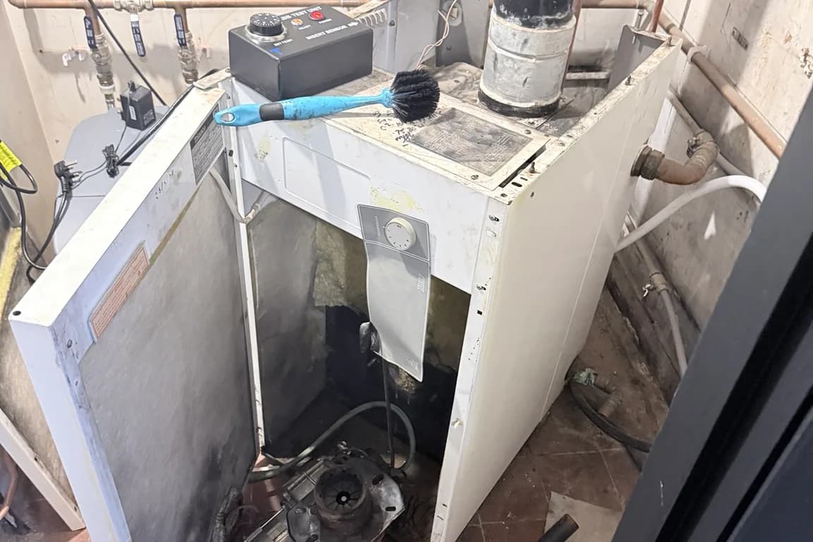 Floor-standing oil boiler opened up during a service, with the burner removed and a cleaning brush on top